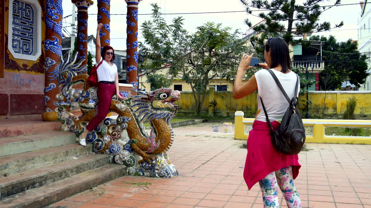 Seorang gadis sedang memotret seorang wanita yang duduk di atas patung naga