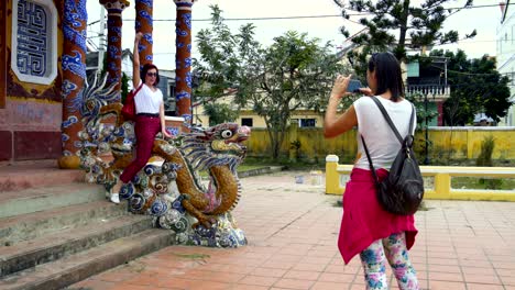 a girl is taking pictures of a woman sitting on a dragon statue