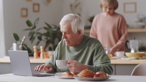 Senior-Man-Browsing-the-Web-on-Laptop-and-Having-Tea