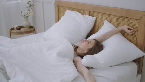 smiling woman waking up. teen hispanic woman wakes up at home. young girl stretching after awake starting a new day with energy and vitality on bed near window in bedroom at morning back view.