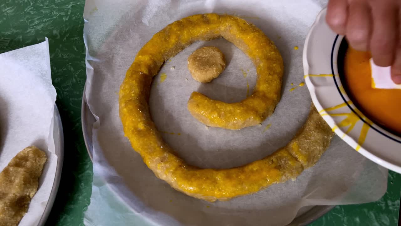 Close up of woman's hands brushing egg wash onto a traditional Italian cake, the Torciglione or tortiglione before baking. For cooking or holiday content