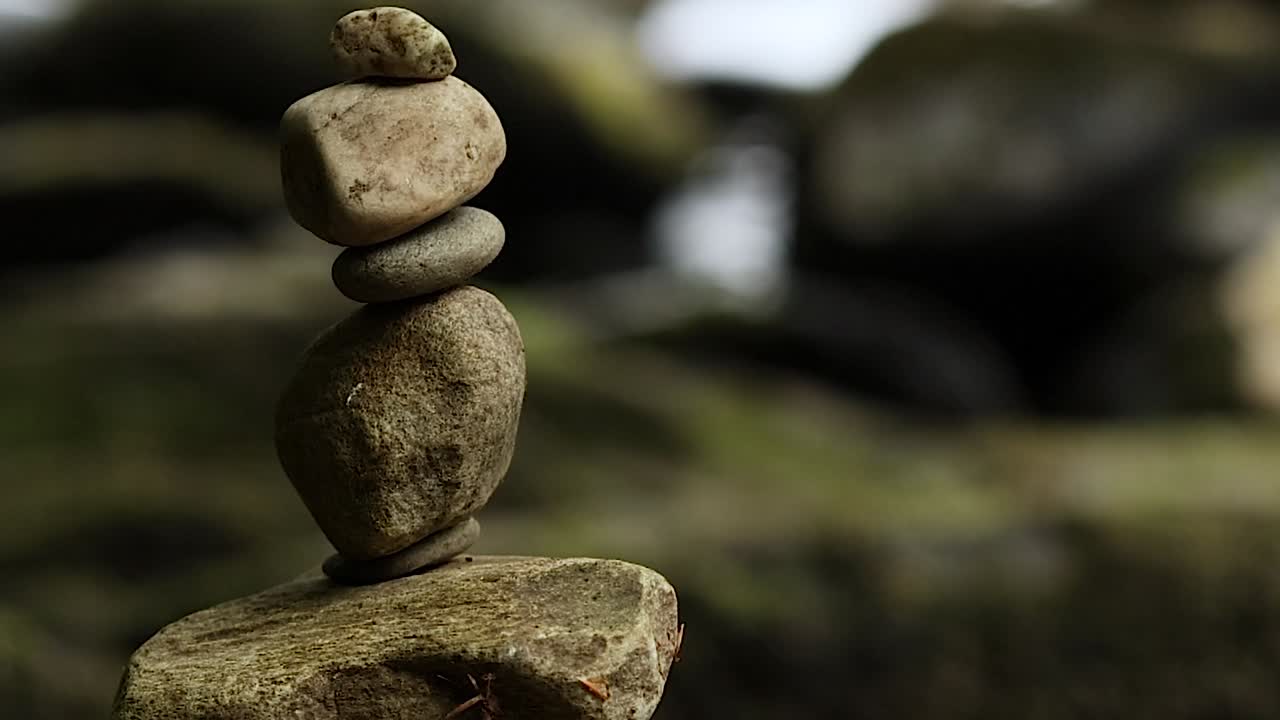 Una pila verticale di sassi di fiume bilanciati si erge al centro su uno sfondo naturale con un delicato effetto bokeh.