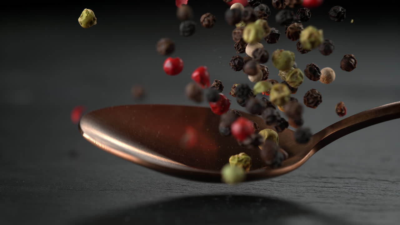 Colorful Peppercorn Mix on a Copper Spoon Falling onto Stone Tabletop in Slow Motion and Macro