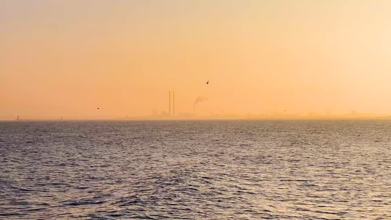 Poolbeg Towers at Sunset with Light Fog, Orange Sky, and Birds Flying Over the Irish Sea