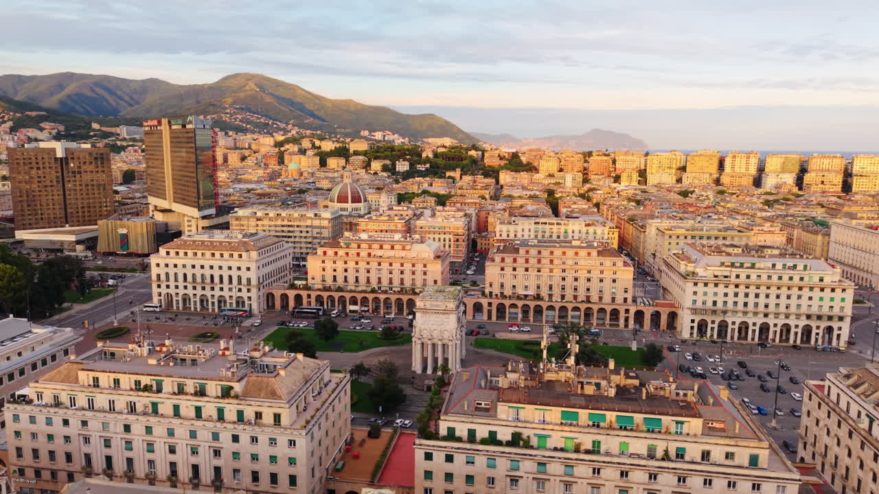 Drone orbit over Piazza della Vittoria in Genoa, showing symmetrical buildings and cityscape glowing in golden hour light