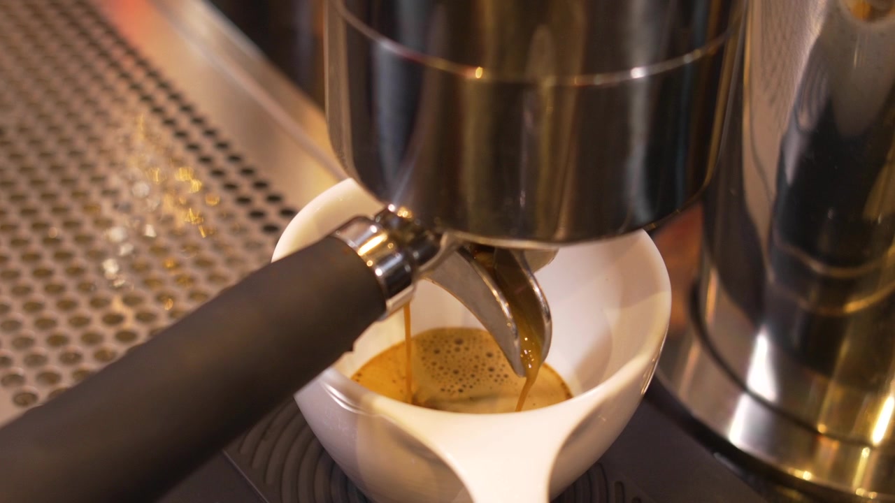 Caffè espresso fresco estratto da un portafiltro professionale in una tazza di ceramica bianca da una macchina da caffè in acciaio inossidabile, in un bar di caffè speciali.