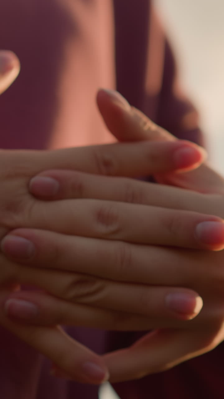 vista de cerca de la mano de una persona con ropa marrón trabajando en el estiramiento de la muñeca con los dedos entrelazados, con la luz del sol creando un reflejo brillante en las manos