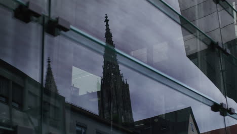 Das-Berühmte-Ulmer-Münster-Spiegelt-Sich-In-Einem-Glasfenster,-Die-Kamera-Fährt-Nach-Links