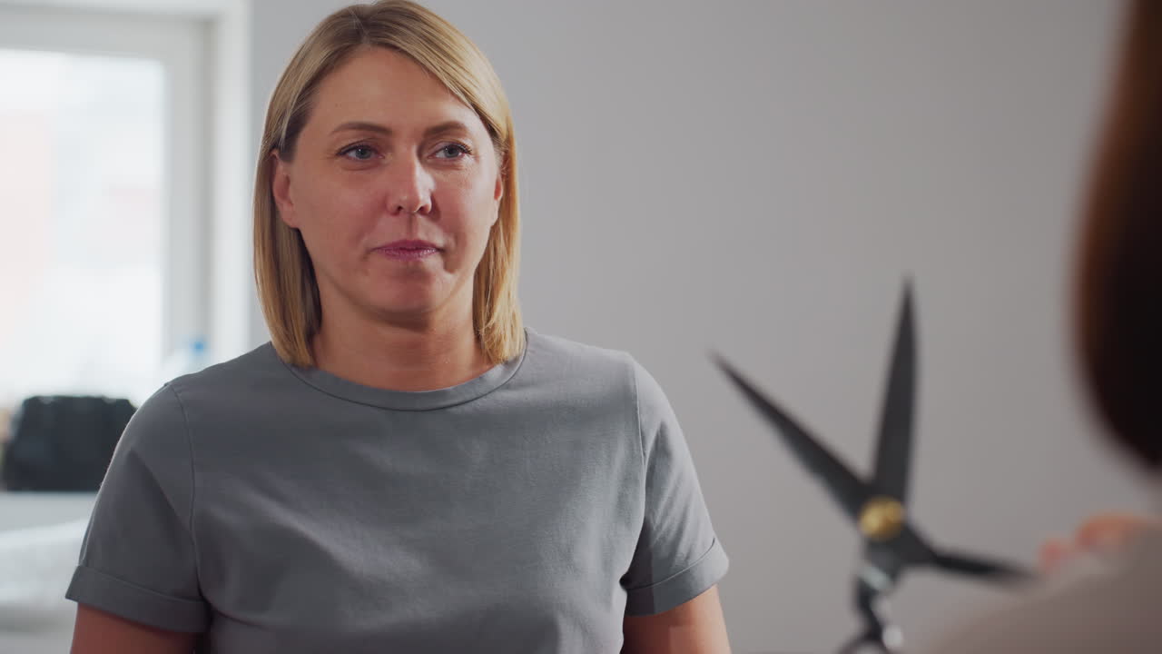 Fashionista playfully acting out shooting and fighting skills with scissors in hands, facing colleague in bright creative workspace with fun and cheerful expression, enjoying lively playful moment