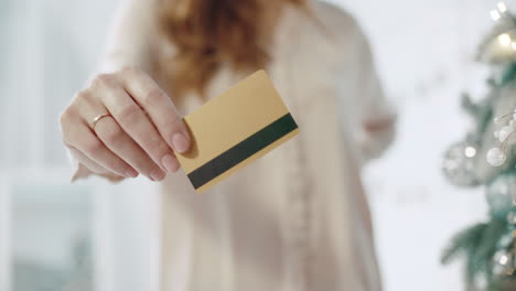 mano de mujer de primer plano mostrando tarjeta de crédito en la habitación decorada de navidad.