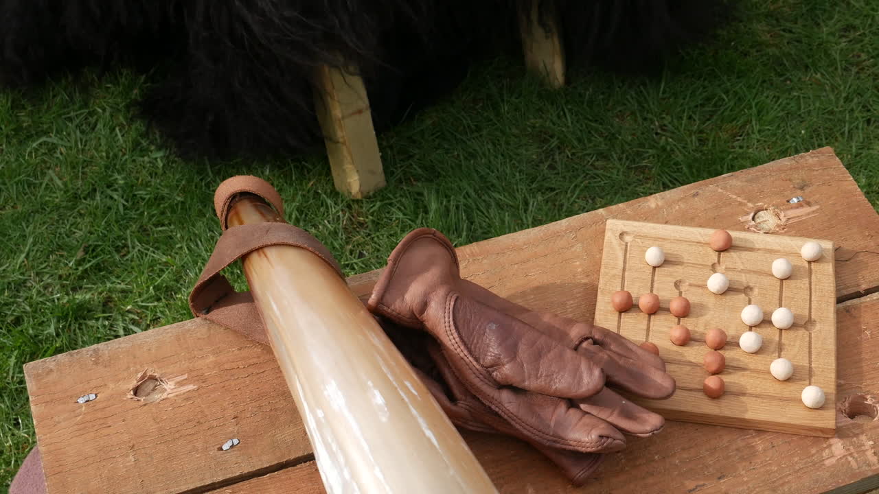 Medieval board game with wooden pieces on a rustic table, next to a horn and leather gloves, evoking historical viking leisure