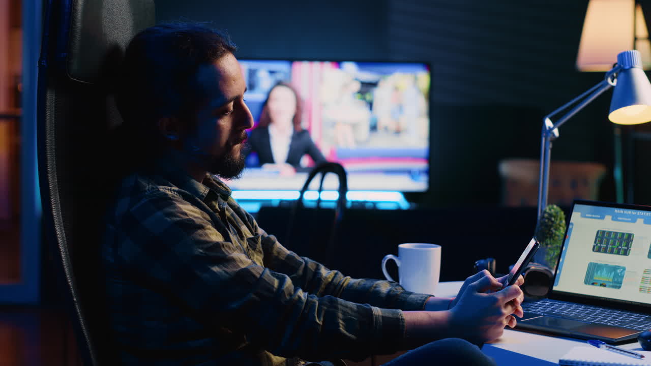 Man takes break from checking financial graphs on laptop, playing games on phone