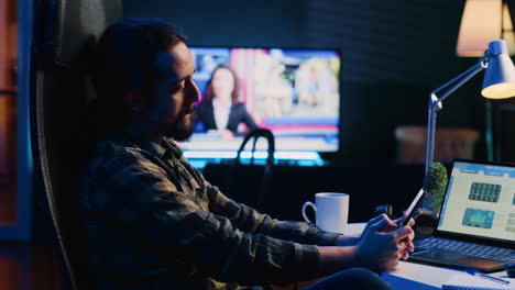 Man-takes-break-from-checking-financial-graphs-on-laptop,-playing-games-on-phone