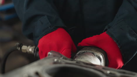 close-up of hands in red gloves working on an engine block in a mechanical workshop, industrial workspace filled with automotive parts and tools