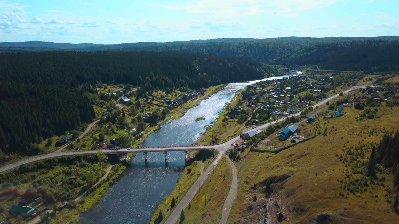 Ilmakuva joesta, sillasta ja metsän keskellä sijaitsevasta kylästä