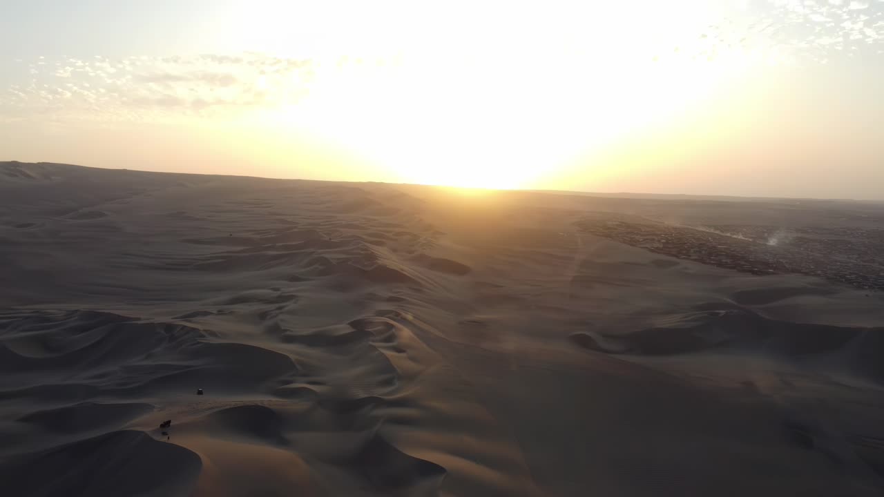 Sweeping aerial of the Huacachina desert oasis surrounded by towering dunes