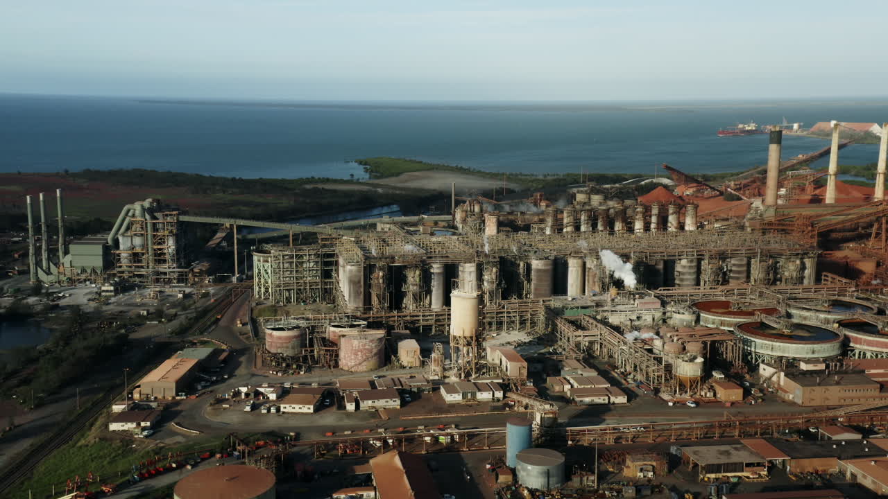 vista aérea de la planta de energía industrial frente al océano azul durante la luz del sol - producción de energía con chimeneas, reactor y almacenamiento