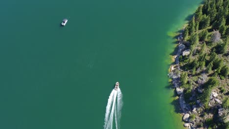 Vista-Aérea-De-Pájaro-De-Un-Barco-Que-Navega-A-Lo-Largo-De-La-Costa-De-Un-Lago-Azul-Claro