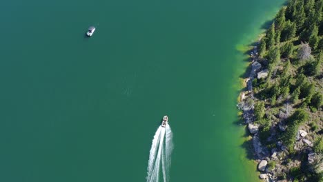 vista aérea de pájaro de un barco que navega a lo largo de la costa de un lago azul claro