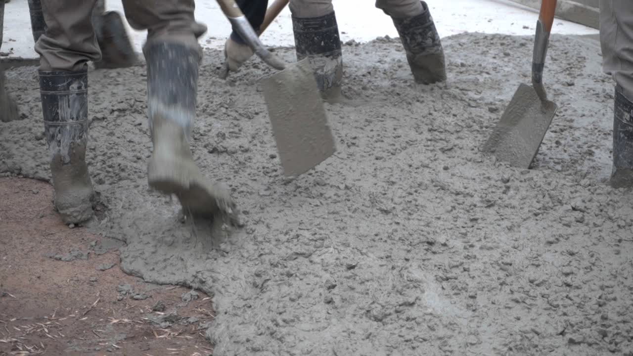 A group of workers with shovels work with their feet on wet concrete paving a road