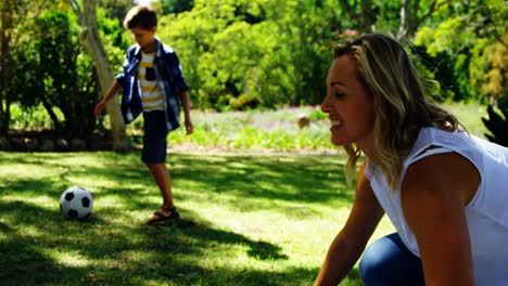 mother spreading the picnic blanket and son playing football in park 4k