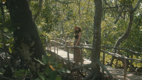 slow motion of an attractive caucasian woman wearing a straw hat looking out and enjoying the forest from a wooden bridge