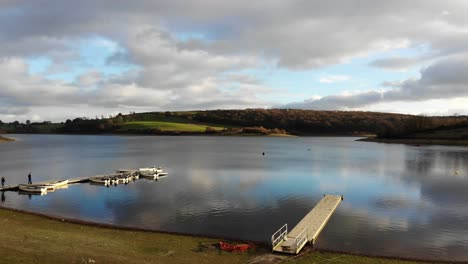 aerial flying over foreshore towards pier with empty boats moored at wimbleball lake on exmoor in somerset