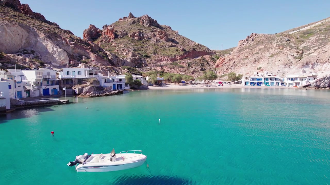 Vista aerea del pittoresco villaggio di pescatori di Firopotamos a Milos, Grecia, con rimesse per barche imbiancate a calce, una chiesa sulla scogliera e barche su acqua turchese. Ripresa drone 4k con avvicinamento