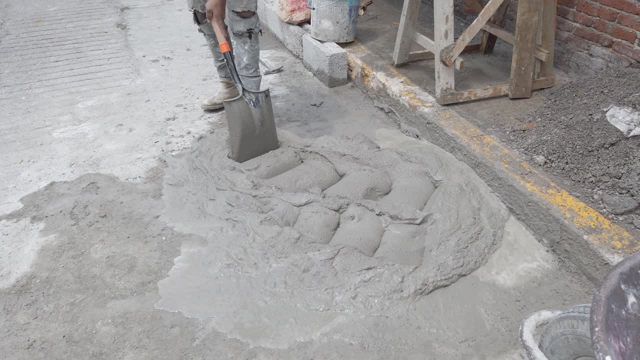 Worker mixes wet cement manually with shovel on street construction site
