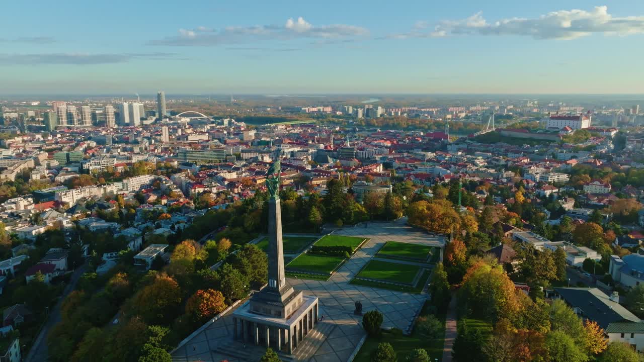 Aerial view of Bratislava, Slovakia at sunrise featuring the iconic Slavin monument, Bratislava Castle, and the city’s skyline with autumn trees and modern buildings