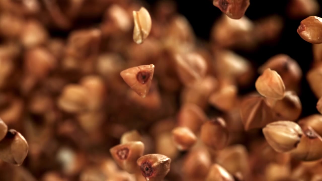 Grani di grano saraceno crudo che cadono al rallentatore su uno sfondo nero