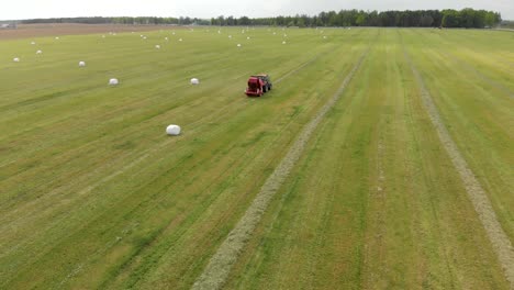 a red tractor collects hay and presses it into white bales using a baler, shot from above