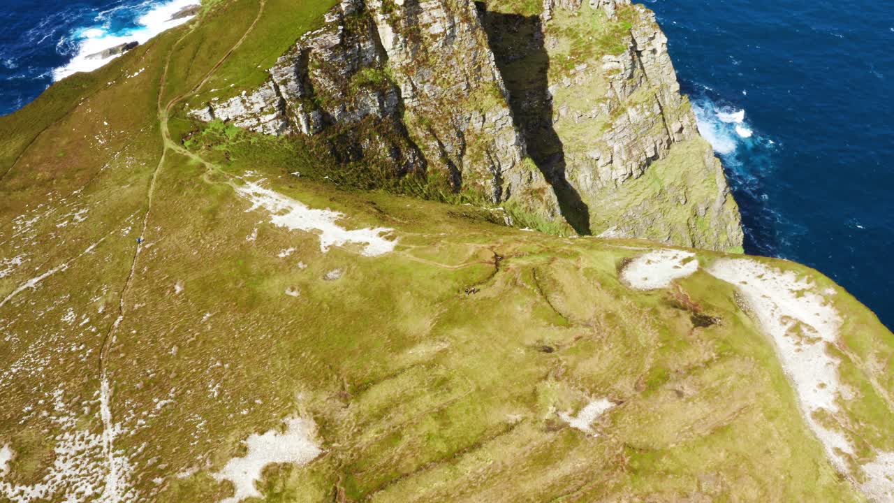Orbiting aerial view of hikers walking the green clifftop of Horn Head with ocean in the background