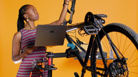 Técnico-Con-Portátil-En-Mano-Analizando-Bicicleta-Rota-Sobre-Fondo-De-Estudio