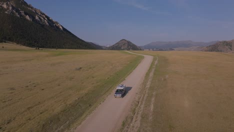 a lone vehicle drives on a dirt road through a vast open landscape under a clear blue sky