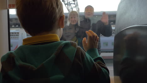vista trasera de un niño mirando por la ventana desde el tren y despidiéndose de sus abuelos balanceando los brazos