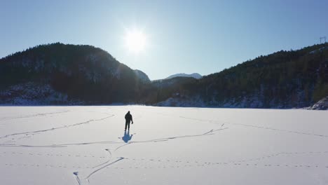 Luftbild,-Das-Einer-Mannsilhouette-In-Strahlender-Sonne-Folgt,-Eislaufen-Auf-Dem-Hintergrund-Der-Gefrorenen-Seeberge