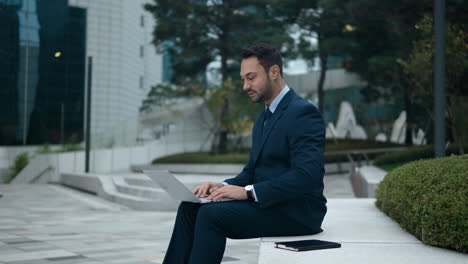 businessman sitting in courtyard, typing on laptop computer