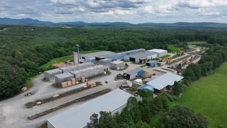 Aerial approaching shot of an industrial facility in rural Virginia, surrounded by dense forest and open fields. Scenic Blue Ridge Mountains in distance under cloudy summer skies. Summer day in va