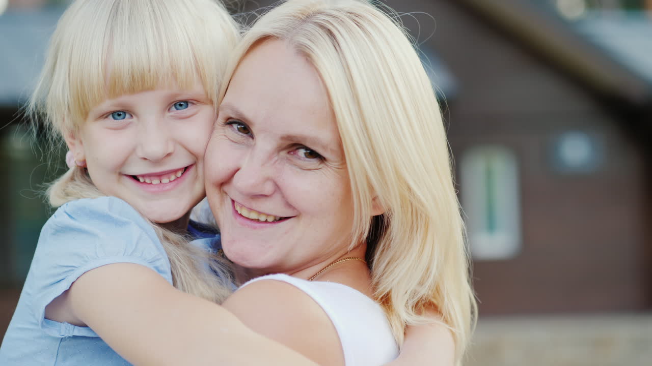 Porträt einer Mutter mit kleiner Tochter, die sich vor dem Hintergrund ihres neuen Zuhauses umarmen.