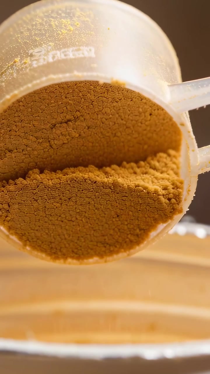 Vertical video: Tilting clear measuring scoop pouring brown powder into bowl on counter for recipe