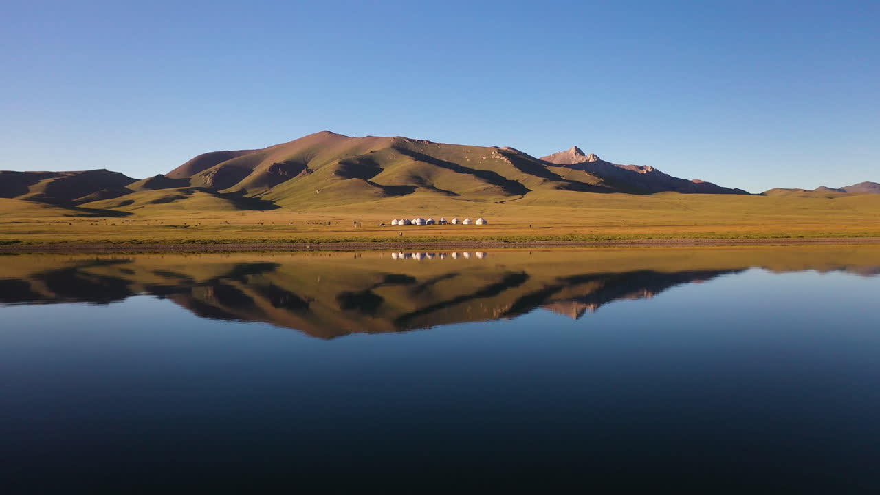 toma épica de drones de un pequeño pueblo de yurtas al lado del lago song-kol en kirguistán, con reflejo en el agua