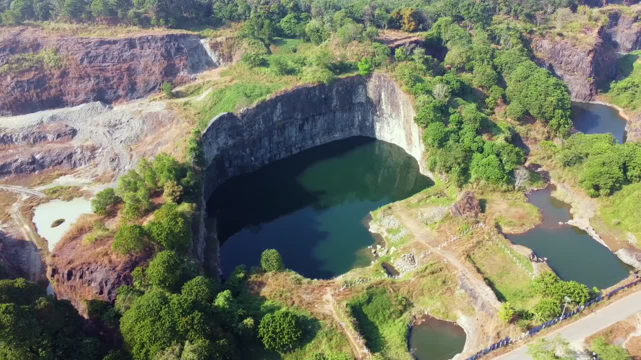 Aerial view of an abandoned rock quarry in India with water-filled pits, rugged cliffs and lush greenery. Ideal for themes on mining, geology, environment, terrain, industrial sites, and nature