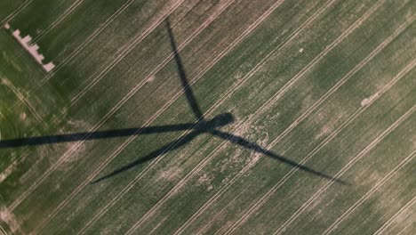 a movie shot from a drone, the shadow of a windmill in the field, the camera is rotating