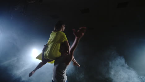 Two-dancers-a-man-and-a-woman-run-to-each-other-and-a-male-partner-raises-a-woman-in-a-yellow-dress-in-her-arms-and-rotates-in-the-air-performing-top-support.