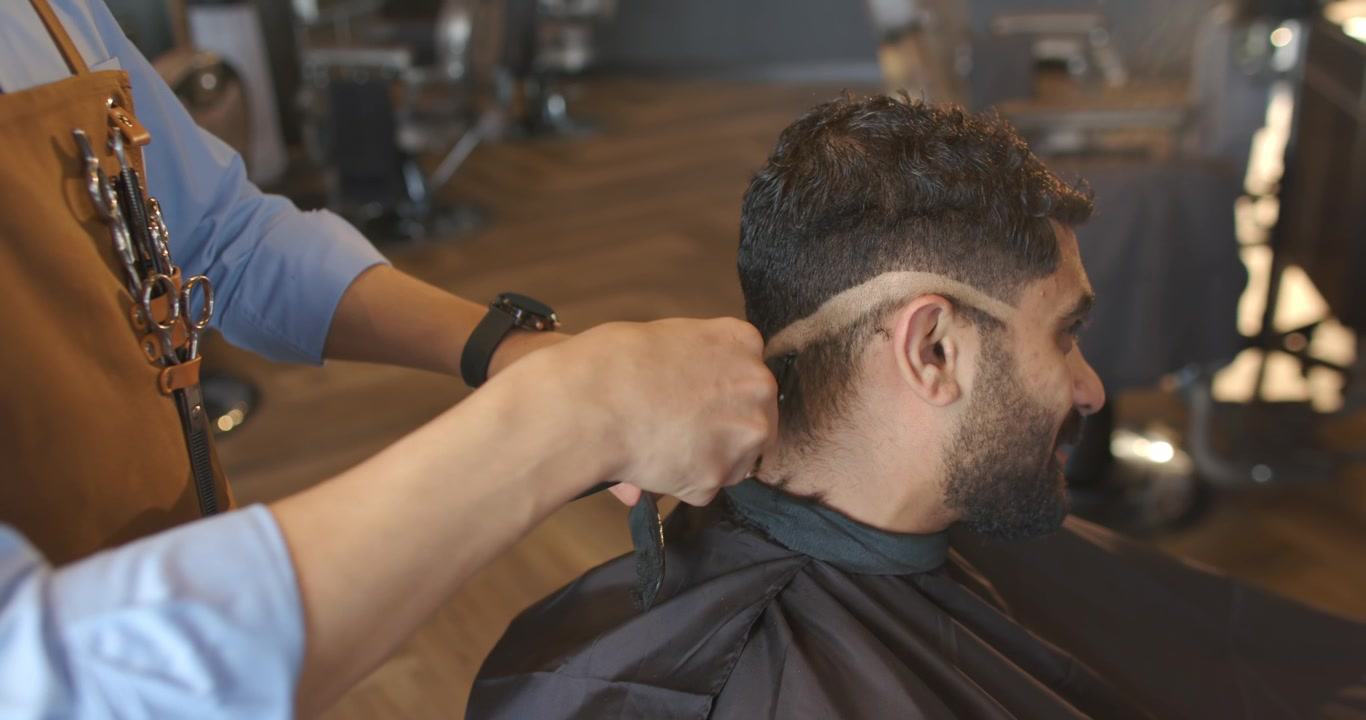 Afroamerikansk frisør lægger sort kappe på kunde, klipper nakken i en fade-frisure i salonen, med plads til tekst
