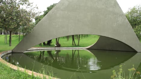 Long-shot-of-an-egret-walking-at-the-grass-around-a-lake-in-an-urban-area-with-a-beautiful-monument