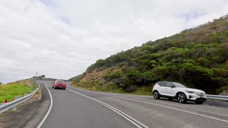vehicles navigate winding coastal roads with lush greenery and overcast skies, capturing the essence of a scenic drive