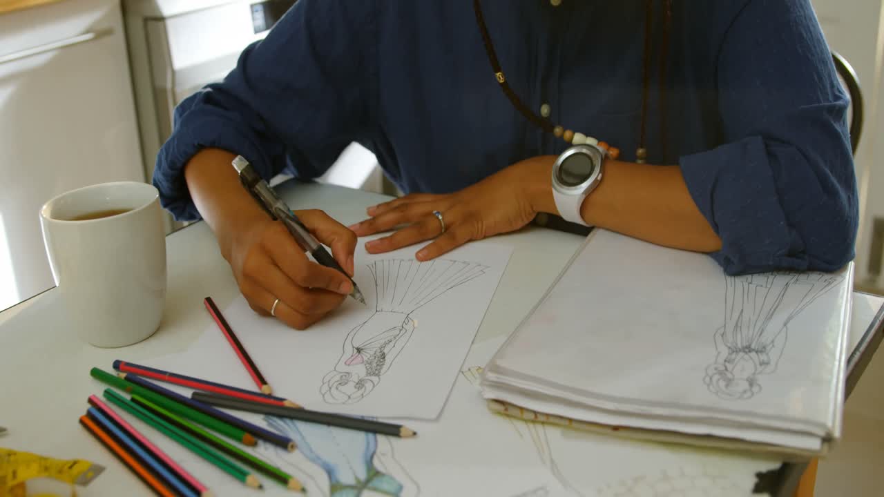 High angle view of young black female fashion designer drawing sketches of dress at dining table 4k