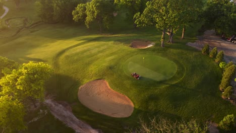 lawn mowing tractor trimming grass at sunset on a golf course